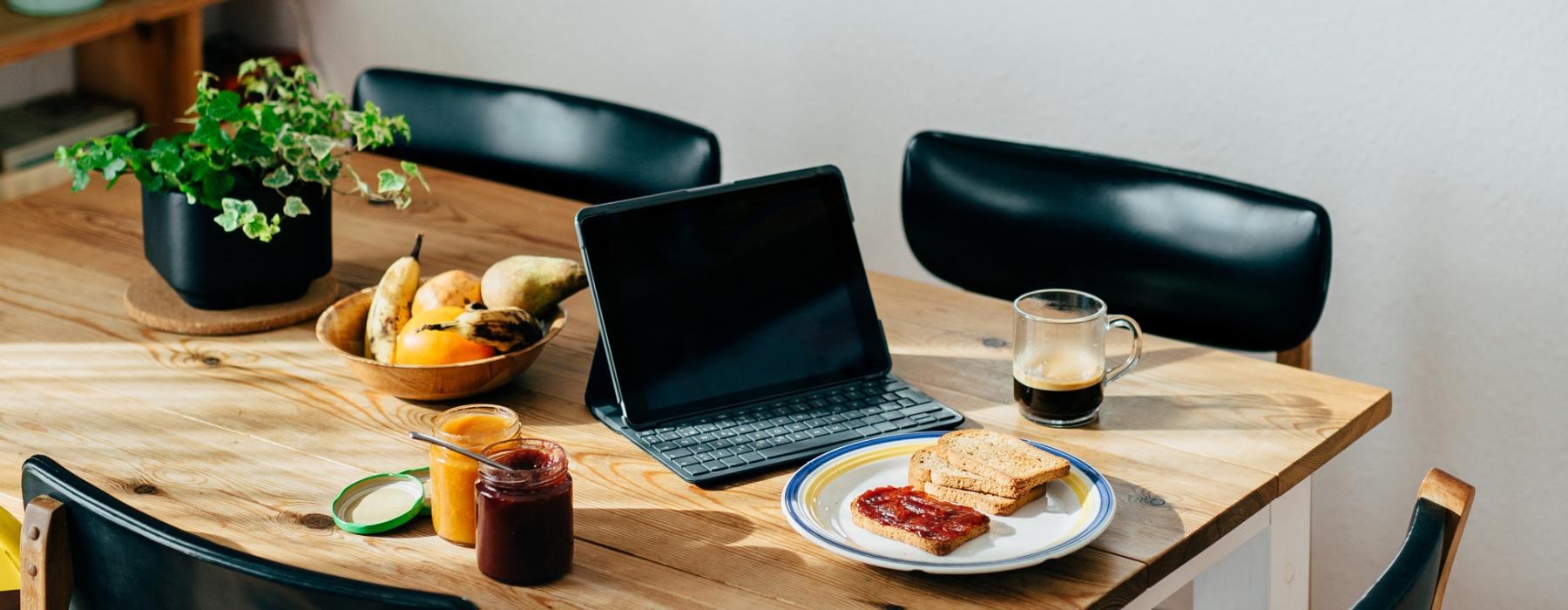 breakfast and a laptop on a dining table in the sunlight